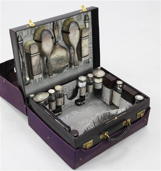 An early 20th century leather travelling toilet case containing twenty engine turned silver mounted jars etc. by Edwards & Sons.